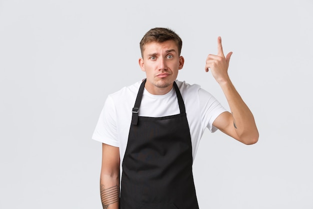 Empleados, tiendas de abarrotes y concepto de cafetería. Barista molesto y preocupado, gerente del café regaña al camarero por cometer un error estúpido, señalar la sien, acusar a alguien loco