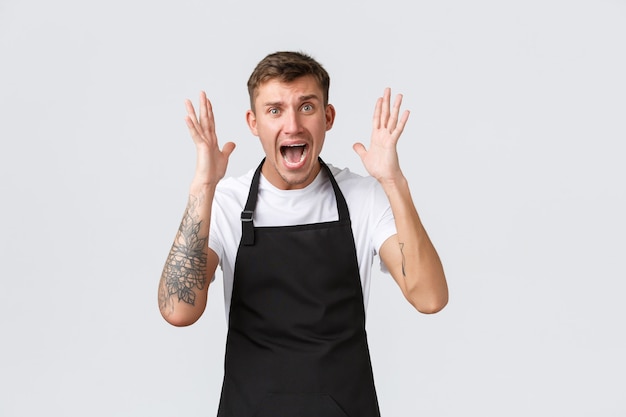 Empleados, tiendas de abarrotes y concepto de cafetería. Barista sorprendido frente al desastre, dándose la mano cerca de la cara y gritando de desesperación, sintiéndose alarmado, presa del pánico por las malas noticias, fondo blanco