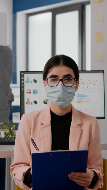 Emprendedor sentado en la nueva oficina normal mirando a la cámara mientras escribe información sobre el estilo de vida