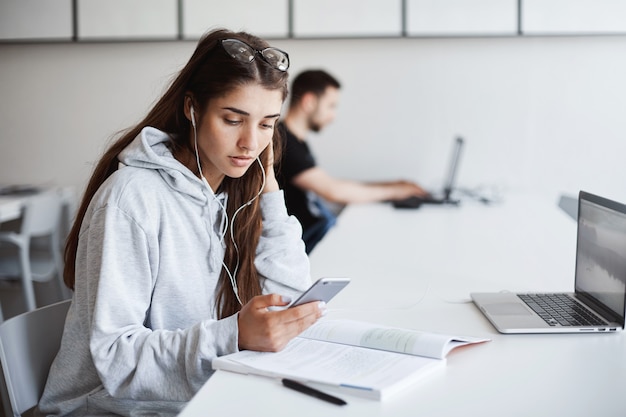 Foto gratuita emprendedora aprendiendo sobre compras en línea usando un teléfono y una computadora portátil. concentrada en su trabajo.