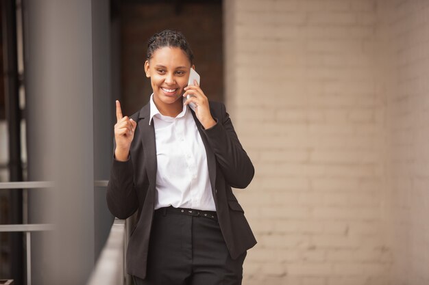 Empresaria afroamericana en traje de oficina sonriendo, parece segura y feliz, exitosa