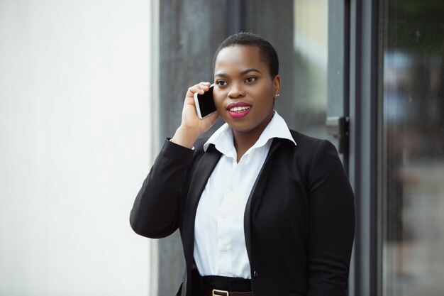 Empresaria afroamericana en traje de oficina sonriendo, se ve confiado y feliz, ocupado