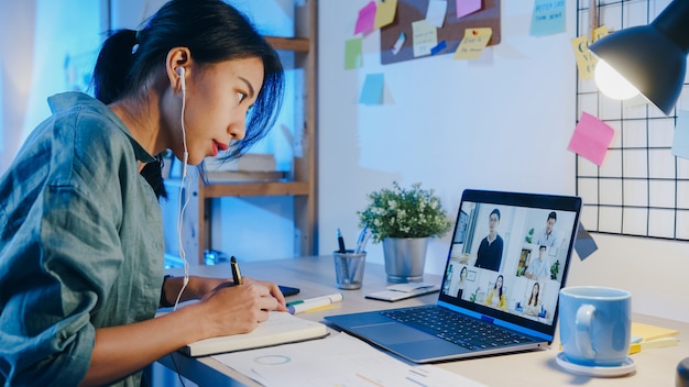 La empresaria de Asia usando la computadora portátil habla con sus colegas sobre el plan en la reunión de videollamada en la sala de estar