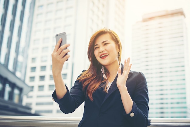 Empresaria asiática joven que usa en smartphone.Young móvil profesional en la ciudad delante de edificio grande.