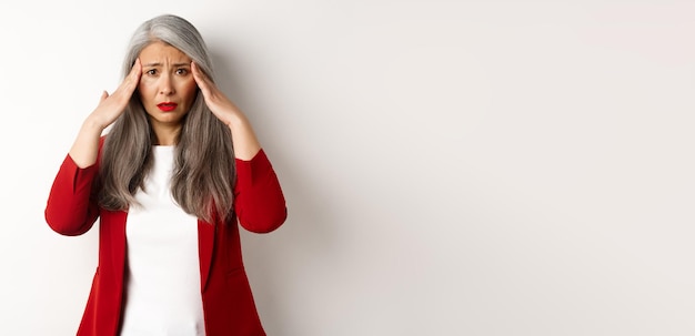 Foto gratuita empresaria asiática con problemas que tiene dolor de cabeza tocando la cabeza y frunciendo el ceño de pie sobre ba blanca