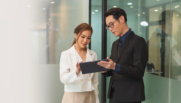 Empresaria asiática sonriente mostrando tableta a su gerente durante una reunión en la oficina