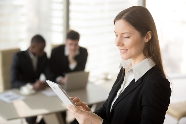 Foto gratuita empresaria atractiva joven que sostiene la tableta, mirando la pantalla