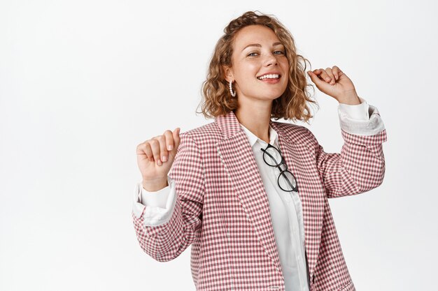 Empresaria bailando sonriendo, divirtiéndose y relajándose, de pie en traje en blanco. Copia espacio