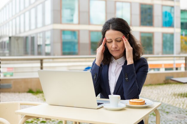 Empresaria cansada usando laptop en café al aire libre