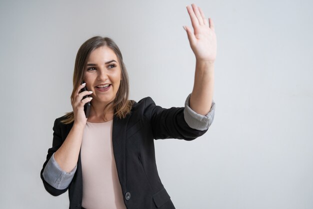 Empresaria caucásica joven feliz con la mano que agita del teléfono