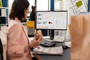 Foto gratuita la empresaria comiendo sabroso sándwich con descanso para comer trabajando en la oficina de la empresa comercial durante el almuerzo para llevar