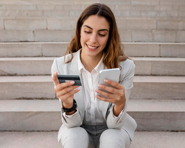 La empresaria de compras en línea con un teléfono inteligente y una tarjeta de crédito mientras está sentado en las escaleras