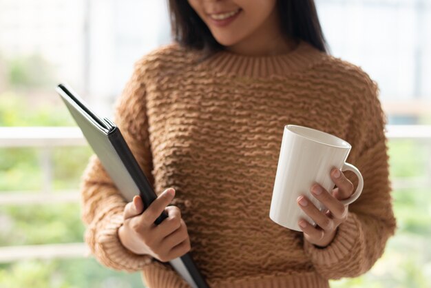 Empresaria confiada contenta que sostiene la taza y la carpeta