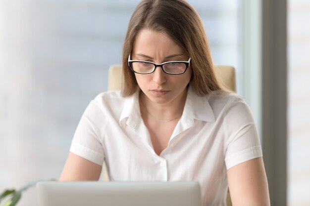 Empresaria confusa ansiosa que tiene problema con el ordenador portátil de la PC, retrato del tiro en la cabeza