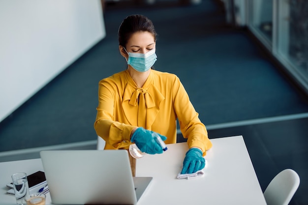 Foto gratuita empresaria desinfectando su escritorio de oficina debido a la pandemia de coronavirus