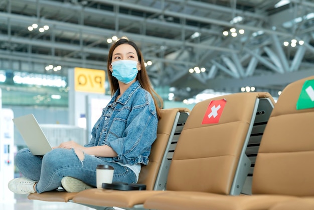 Empresaria de distanciamiento social con mascarilla sentada trabajando con una computadora portátil manteniendo la distancia entre sí para evitar la infección por covid19 durante la pandemia El asiento de la silla vacía la cruz roja muestra una nueva normalidad