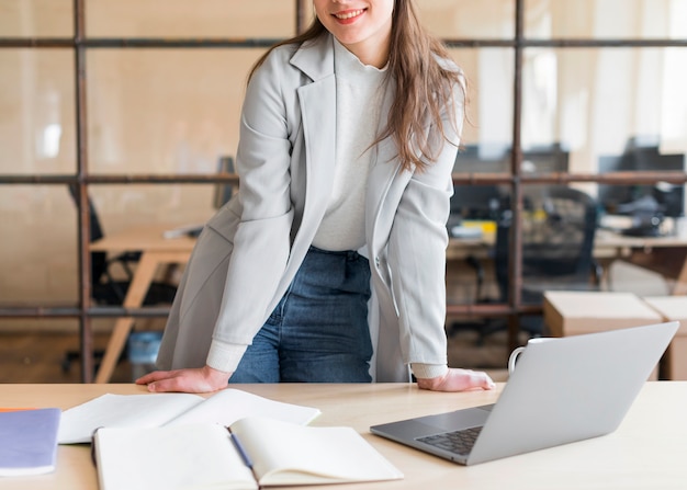 Empresaria elegante sonriente que se coloca delante del ordenador portátil