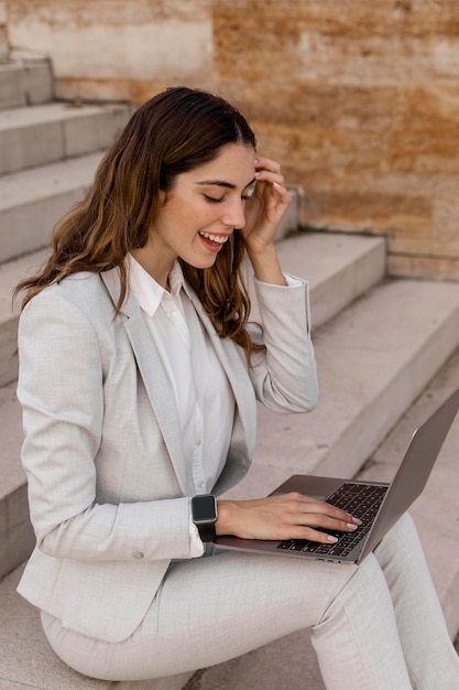 Empresaria elegante sonriente con reloj inteligente trabajando en el portátil al aire libre