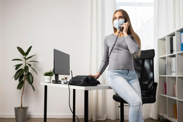 Empresaria embarazada con máscara médica hablando por teléfono