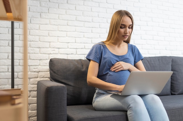 Empresaria embarazada en el sofá trabajando con portátil