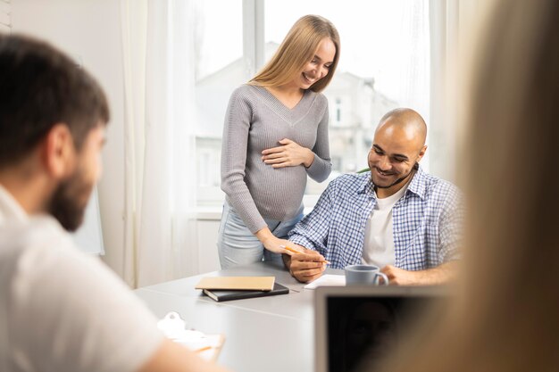 Empresaria embarazada sonriente con compañeros de trabajo masculinos en la oficina