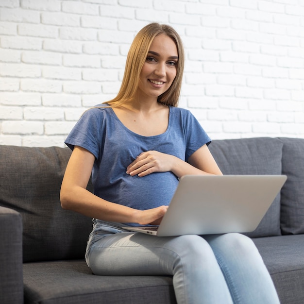 Foto gratuita empresaria embarazada sonriente trabajando en la computadora portátil desde el sofá