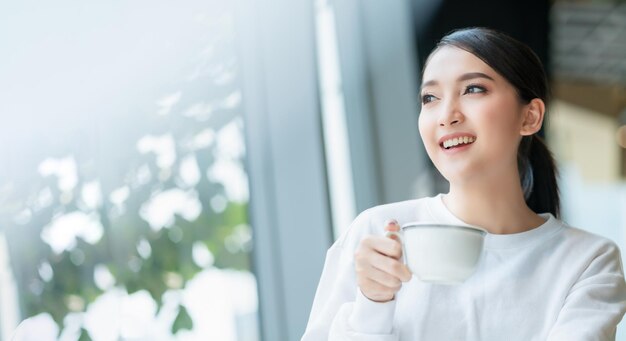 empresaria emprendedora dueña de una empresa atractiva mujer de negocios asiática comunicación con teléfono inteligente y computadora portátil vestido blanco alegre y sonrisa con confianza desenfoque de fondo de la oficina