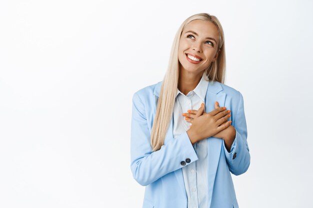 Empresaria de ensueño cogidos de la mano en el corazón sonriendo y mirando a un lado imaginando algo imaginando un momento romántico de pie sobre un fondo blanco