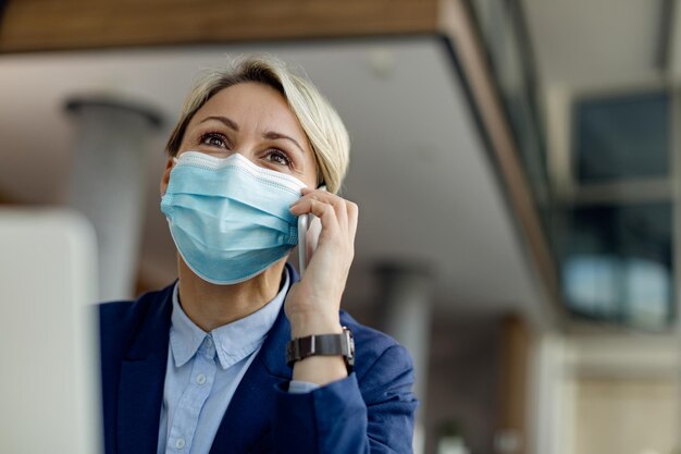 Empresaria feliz con mascarilla protectora mientras habla por teléfono en la oficina