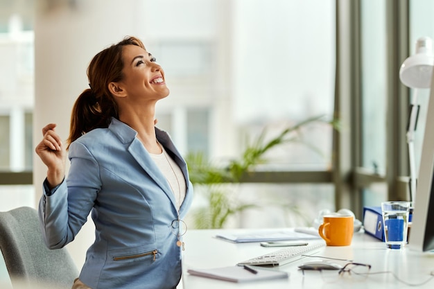 Empresaria feliz mirando hacia arriba mientras se estira en la oficina