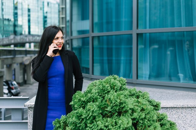 Empresaria feliz que habla en el teléfono móvil fuera del edificio de oficinas