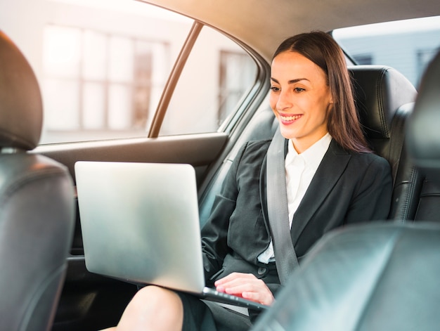 Empresaria feliz que viaja en coche usando la computadora portátil