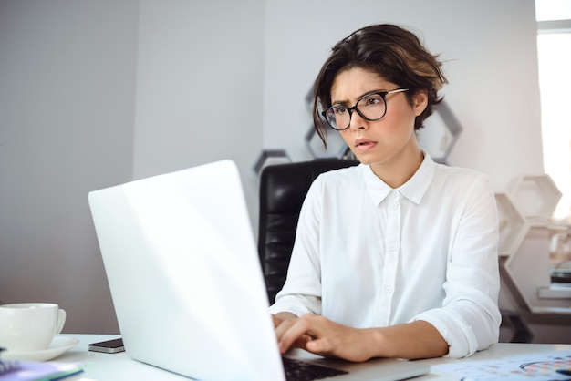 Empresaria hermosa joven que trabaja con la computadora portátil en el lugar de trabajo en oficina.