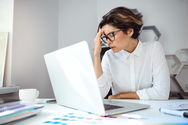 Empresaria hermosa joven que trabaja con la computadora portátil en el lugar de trabajo en oficina.