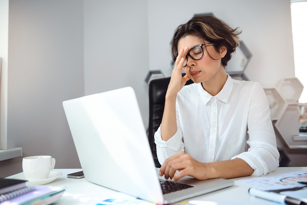 Empresaria hermosa joven que trabaja con la computadora portátil en el lugar de trabajo en oficina.