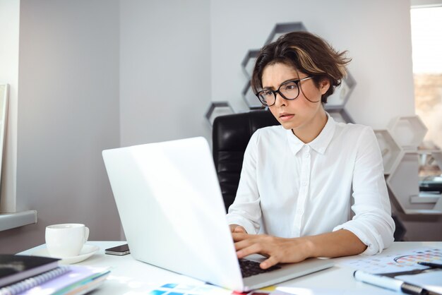 Empresaria hermosa joven que trabaja con la computadora portátil en el lugar de trabajo en oficina.