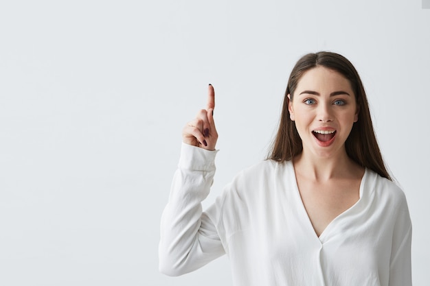 Foto gratuita empresaria hermosa joven sorprendida con la boca abierta que sonríe señalando el dedo para arriba.