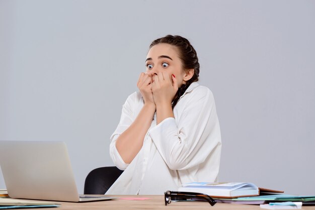 Empresaria hermosa joven sorprendida que trabaja en la computadora portátil sobre la pared púrpura