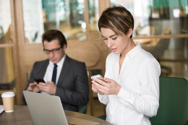 Empresaria y hombre de negocios usando teléfonos móviles para el trabajo en la oficina