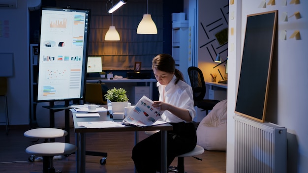 Foto gratuita la empresaria ingrese en la sala de reuniones de la oficina de la empresa a altas horas de la noche sentado en el escritorio a altas horas de la noche trabajando en las estadísticas de análisis de ganancias de marketing