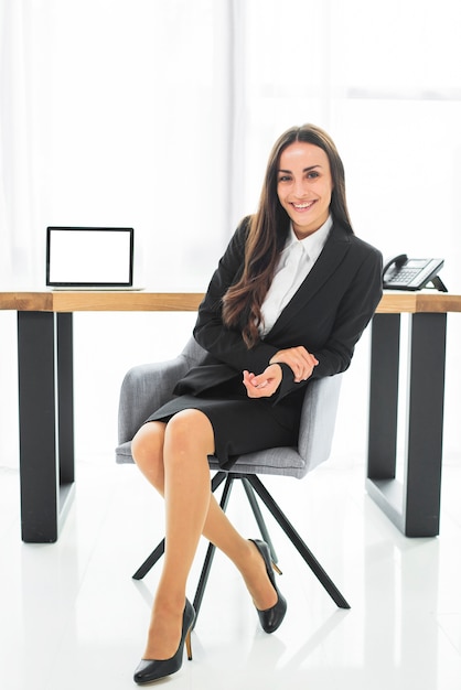 Empresaria joven confiada sonriente que se sienta en silla