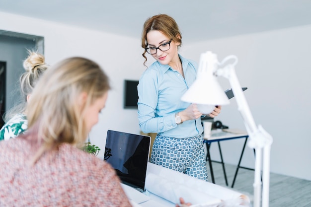 Foto gratuita empresaria joven elegante que mira a dos mujeres que trabajan en el lugar de trabajo