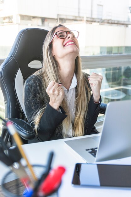 Empresaria joven emocionada que se sienta en el lugar de trabajo