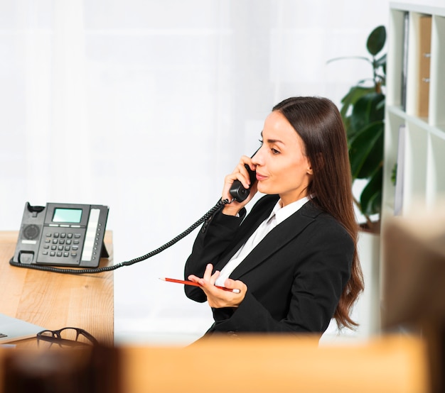 Foto gratuita empresaria joven hermosa que se encoge de hombros mientras que habla en el teléfono