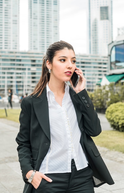 Empresaria joven hermosa que habla en el teléfono móvil con la mano en su bolsillo