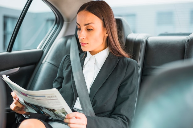 Empresaria joven hermosa que viaja en coche que lee el periódico