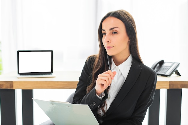 Foto gratuita empresaria joven pensativa con la pluma y el tablero en su mano