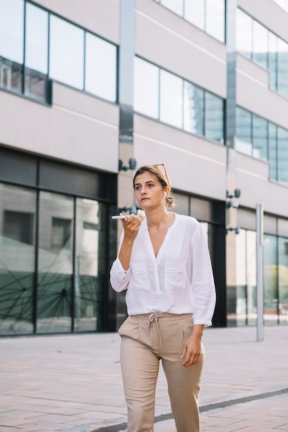 Empresaria joven que camina cerca del edificio de oficinas que habla en el teléfono móvil