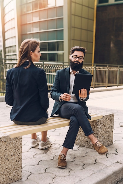 Empresaria joven que mira al hombre de negocios usando la tableta digital que se sienta en banco