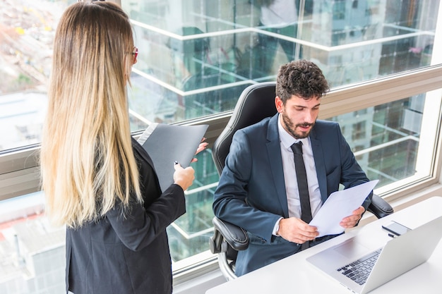 Foto gratuita empresaria joven rubia que se coloca cerca del documento de la lectura del hombre de negocios